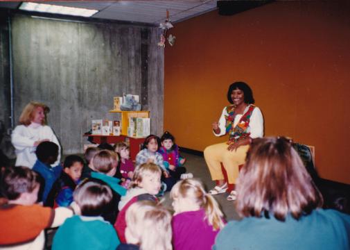 Library storyteller Crystal Sullivan telling a story to a group of children seated on the floor of the library