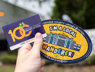 A hand holding a local wanderer magnet and OCLS library card.