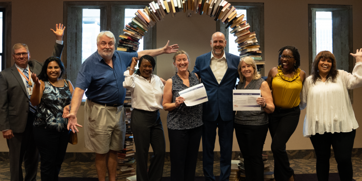 Orange County Library System board of trustees members, library director and others posing in front of the book arch at Orlando Public Library and holding the signed lease agreements for Horizon West and Lake Nona branches