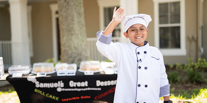 Boy wearing chef's uniform smiling and waving