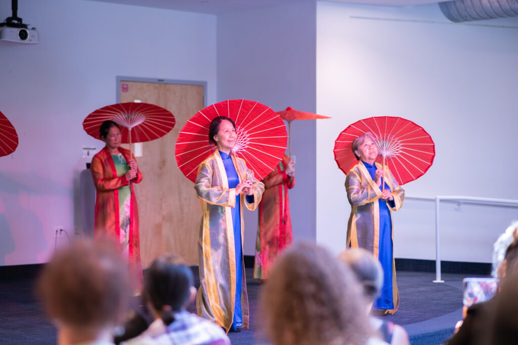 Thuyen May dancers performing with parasols on stage at Chickasaw Branch