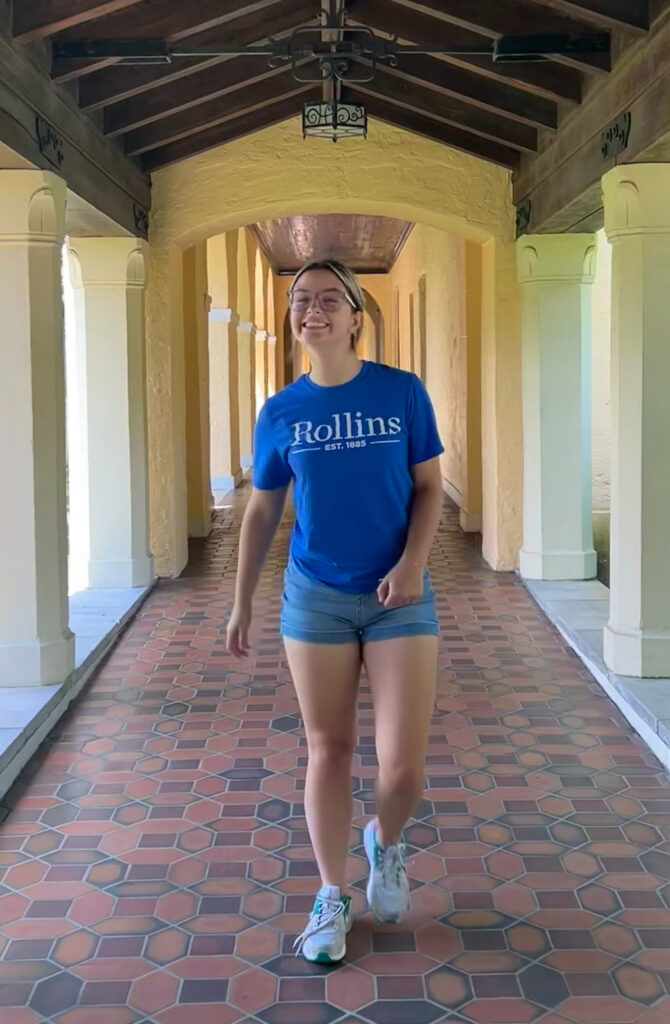 Kaylie Pasternak, wearing a blue Rollins College shirt, walking down tiled hallway